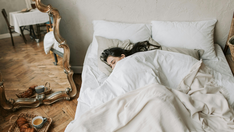 Woman tucked up in a large white bed in a hotel room