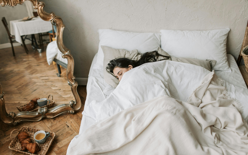 Woman tucked up in a large white bed in a hotel room