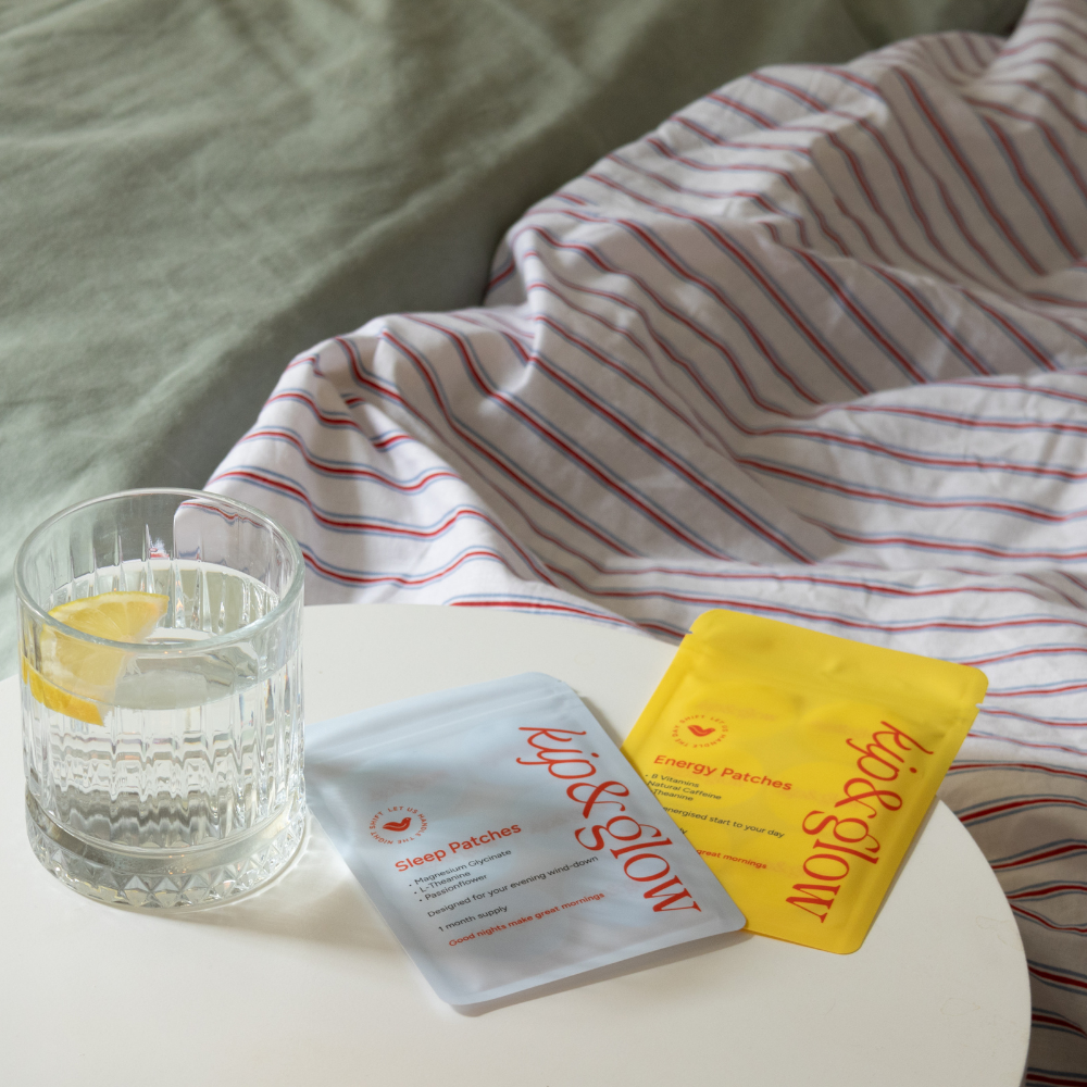 kip&glow Sleep and Energy Patch packets, resting on a white table next to a glass of water with a lemon slice, with a striped blanket in the background.