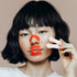 Woman with bobbed dark hair holding up kip&glow nose strip whilst wearing the sleep tape and nose strip